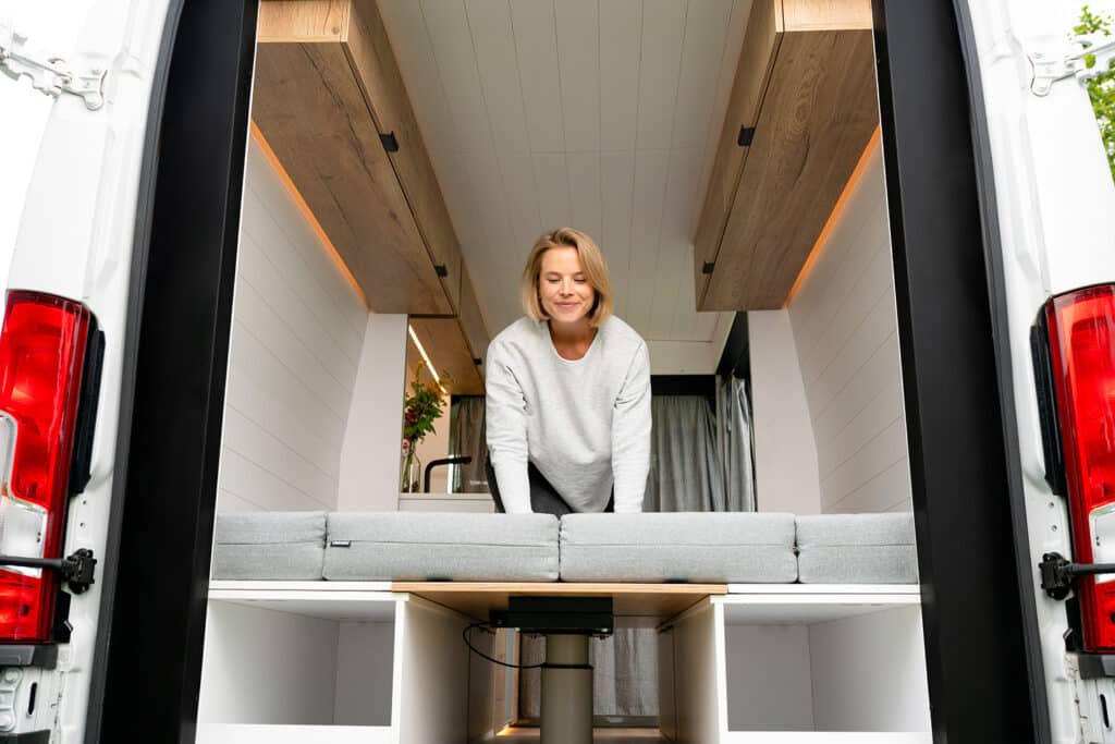 Model converting the bench setup into the queen bed in The Biggie campervan