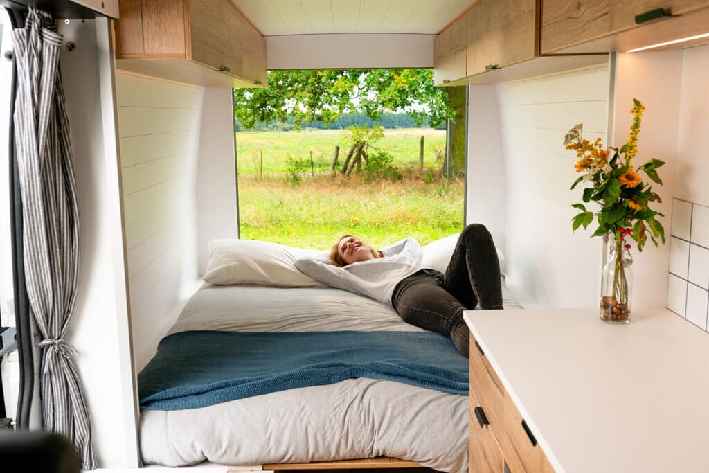 Traveler relaxing on the queen bed inside The Biggie campervan