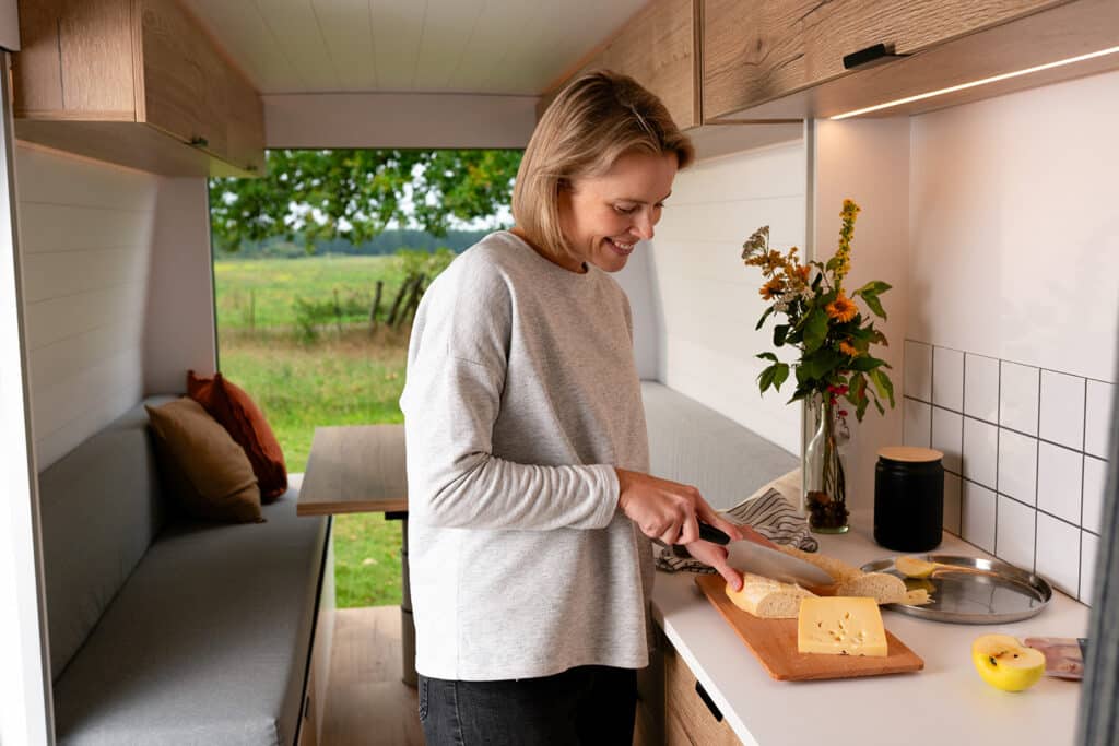 Woman preparing lunch and slicing cheese inside The Biggie campervan kitchen