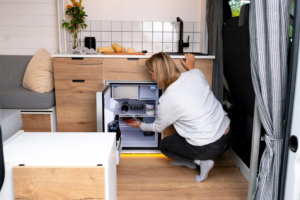 Traveler reaching into the built-in fridge in The Biggie campervan kitchen