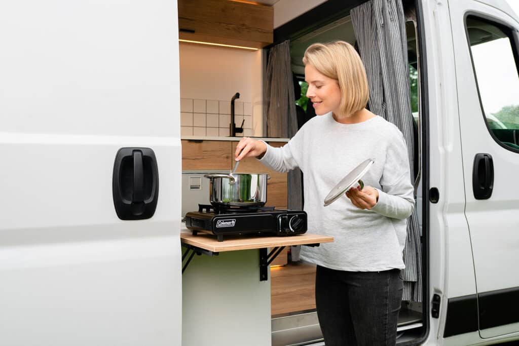Woman cooking on an outdoor grill using the flip-up table on The Biggie campervan
