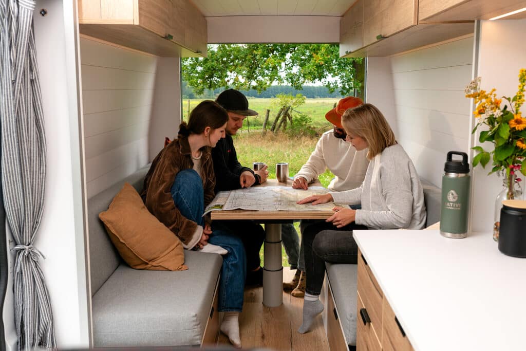 Group of friends reading a map while seated at the table inside The Biggie campervan