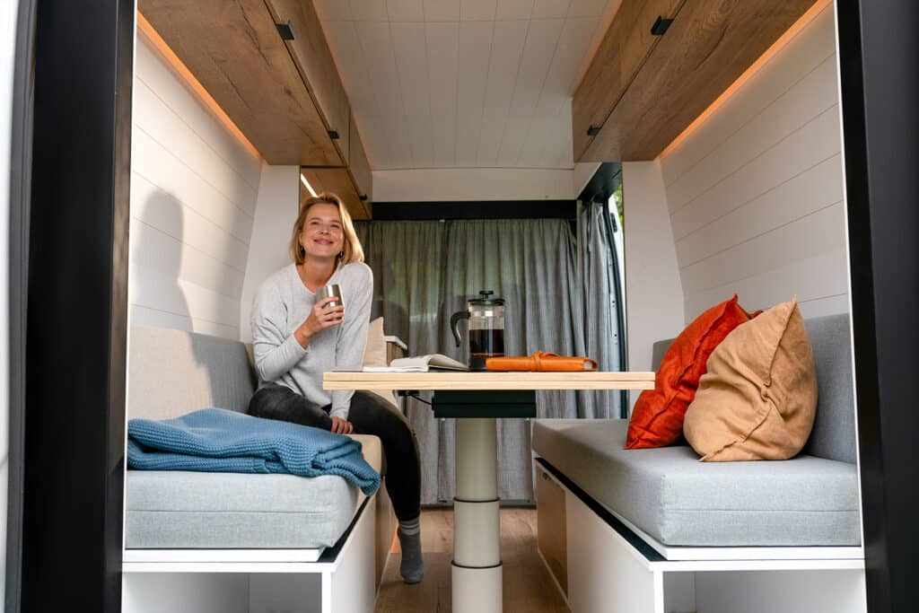 Traveler enjoying coffee on the convertible bench inside The Biggie campervan